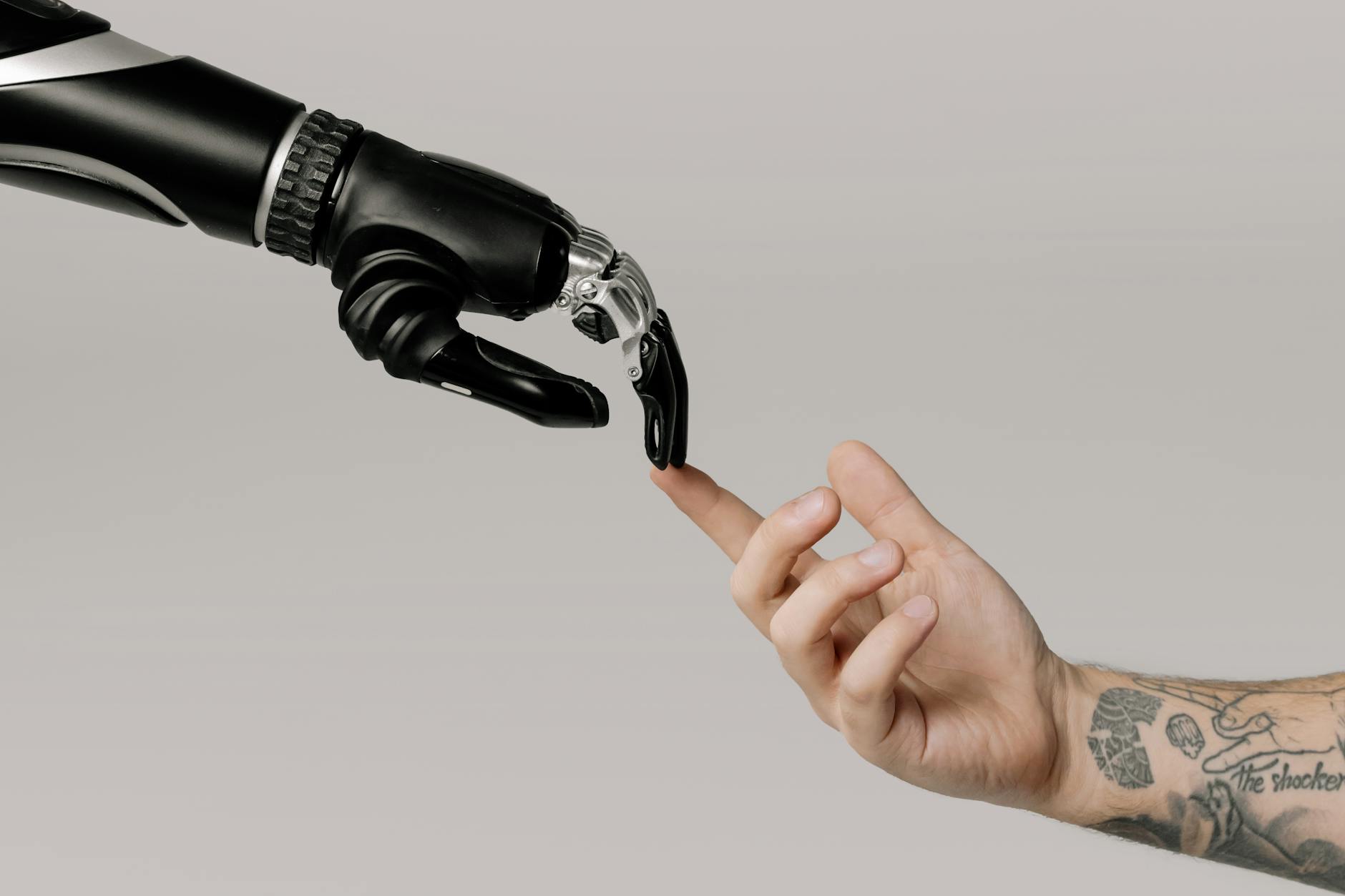 Wytatuowana ludzka dłoń sięga do mechanicznej dłoni robota