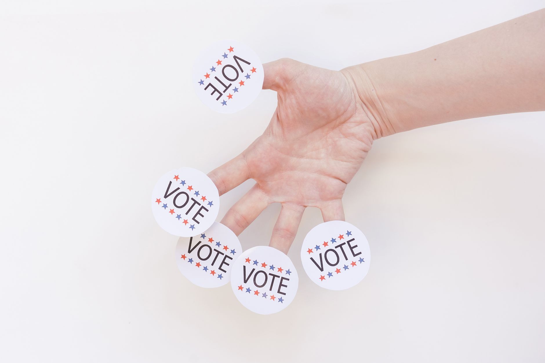 Dłoń trzyma kilka naklejek z napisem Vote na białym tle