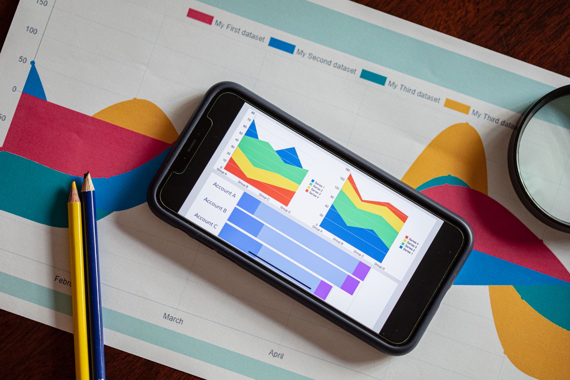 Smartfon z kolorowymi wykresami na tle papierowych grafik analitycznych